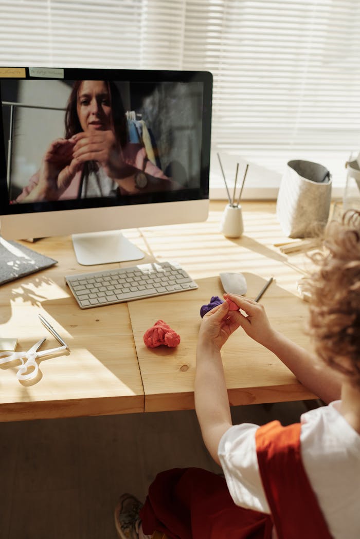 A child engaging in an online arts and crafts class, learning from home with clay and a computer.